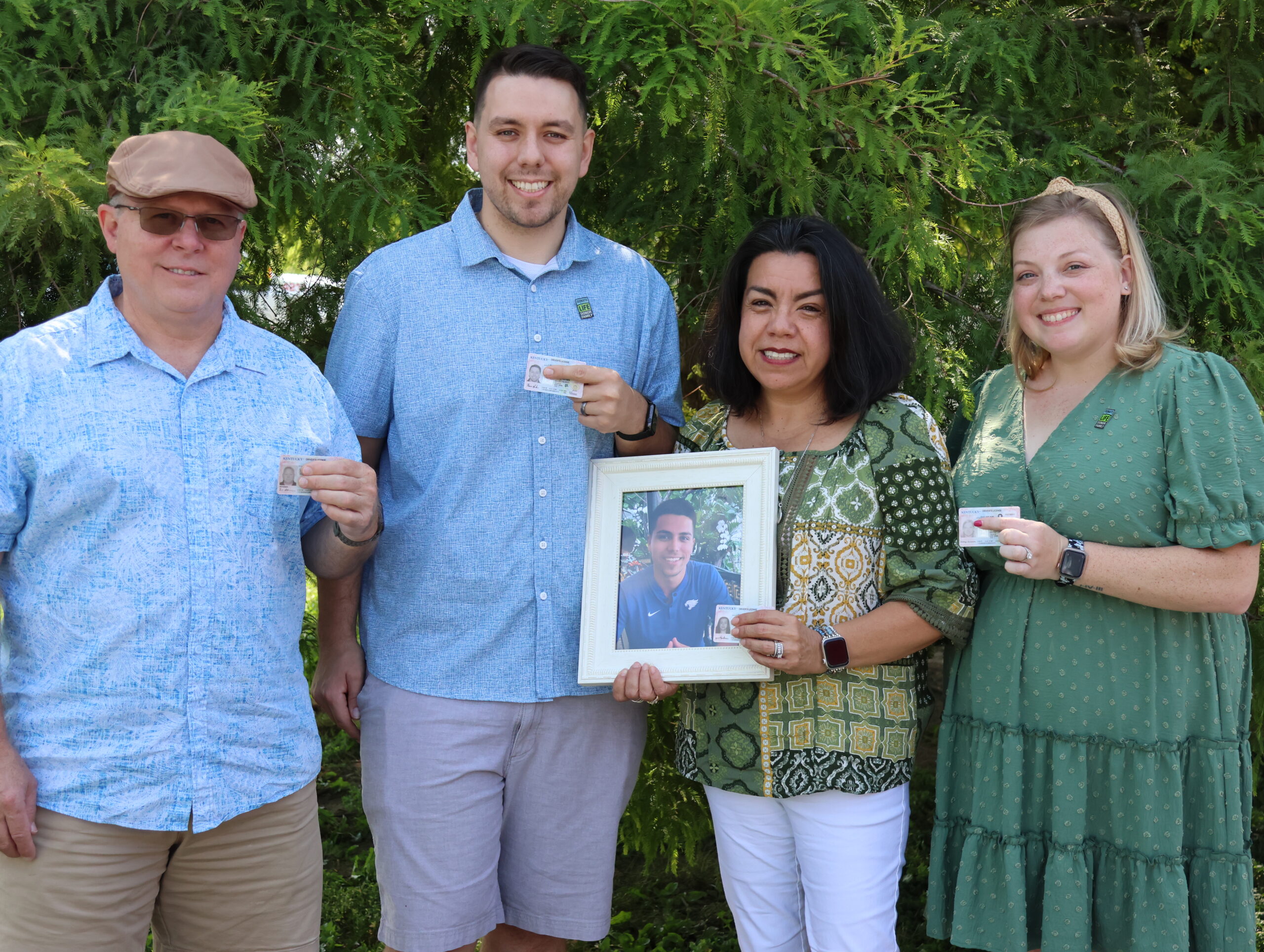 Family posing with picture of son and drivers licenses.