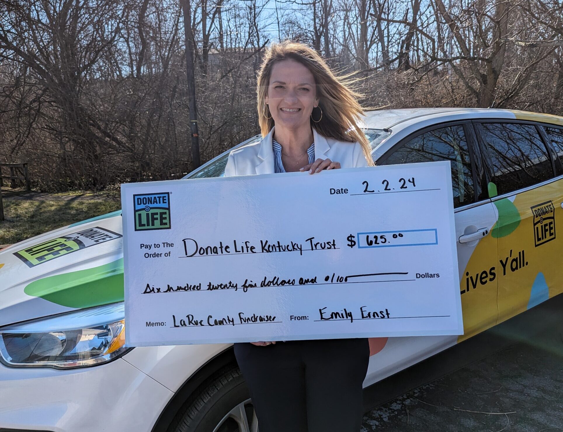 Lady standing in front of Donate Life SUV with a large check